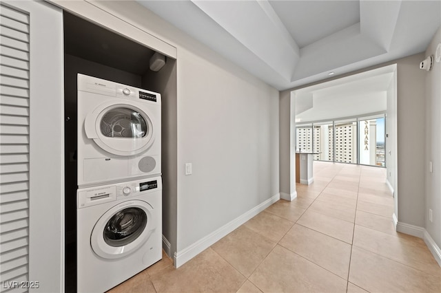 laundry room featuring light tile patterned floors, laundry area, stacked washer and clothes dryer, and baseboards