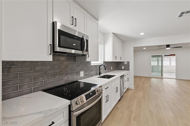 kitchen with light stone counters, light wood-style flooring, a sink, stainless steel appliances, and tasteful backsplash