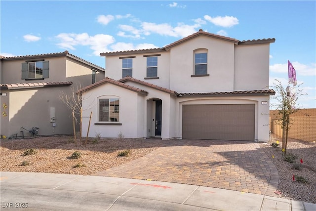 mediterranean / spanish home with decorative driveway, fence, a garage, and stucco siding