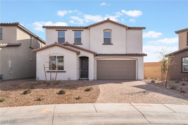 mediterranean / spanish house with decorative driveway, a tile roof, an attached garage, and stucco siding