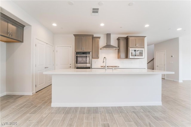 kitchen with visible vents, light wood finished floors, built in microwave, oven, and wall chimney exhaust hood