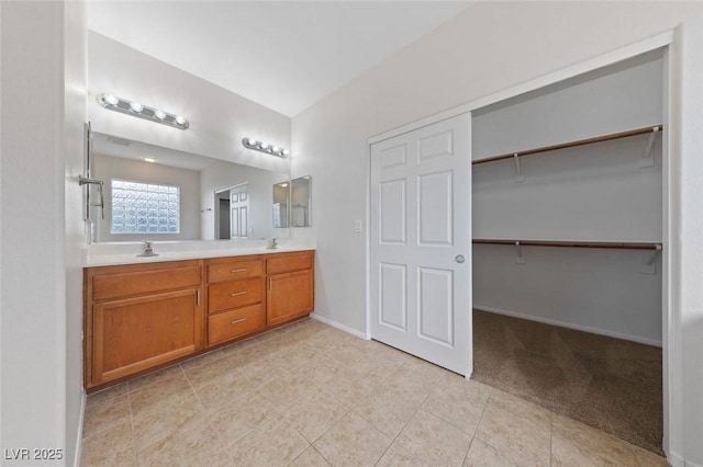 bathroom featuring a walk in closet, double vanity, baseboards, and a sink