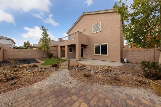 rear view of house featuring a patio area, a fenced backyard, stucco siding, and a balcony