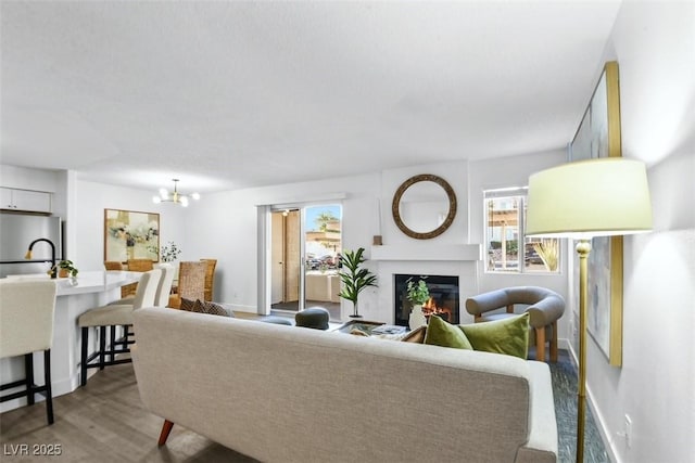 living room featuring a glass covered fireplace, an inviting chandelier, wood finished floors, and baseboards