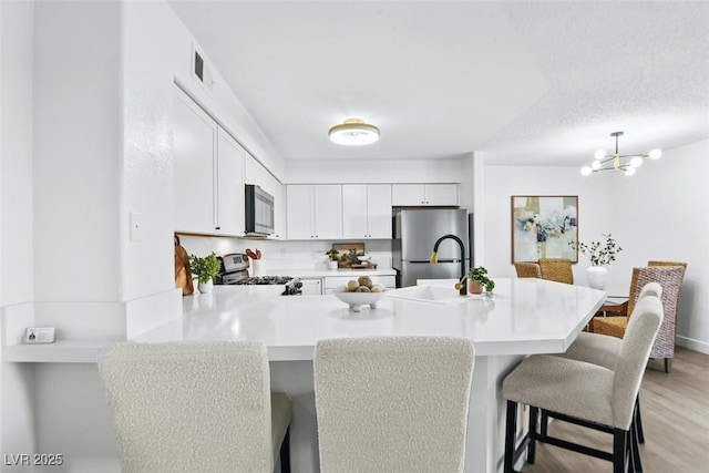 kitchen featuring light countertops, a peninsula, a kitchen breakfast bar, stainless steel appliances, and a sink