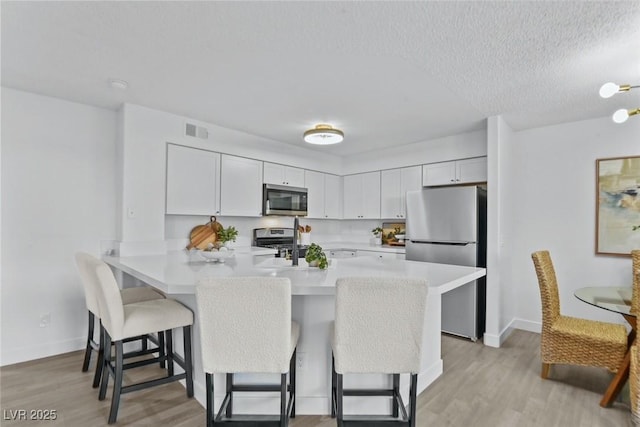 kitchen featuring visible vents, a breakfast bar, stainless steel appliances, light wood finished floors, and light countertops