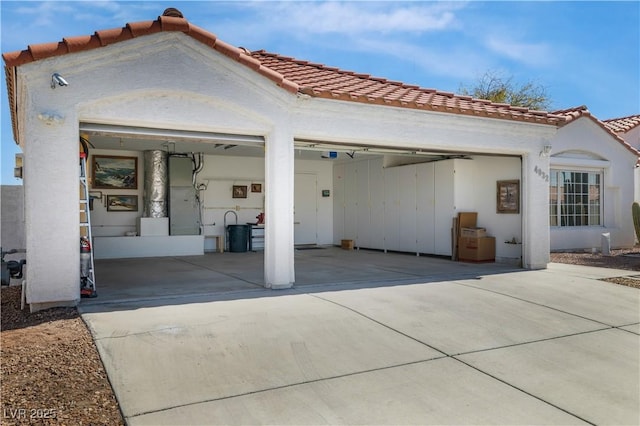 back of property with stucco siding, concrete driveway, an attached garage, and a tiled roof