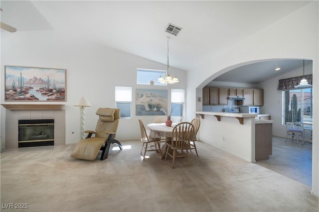 dining space with visible vents, light colored carpet, a tile fireplace, a notable chandelier, and high vaulted ceiling