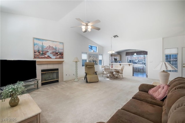 carpeted living room with visible vents, ceiling fan with notable chandelier, a tile fireplace, and high vaulted ceiling