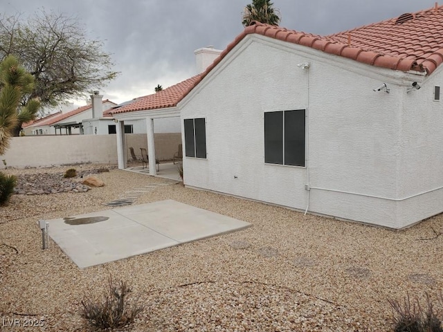 rear view of house featuring a tiled roof, fence, stucco siding, and a patio area