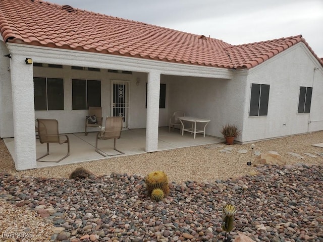 rear view of property featuring a patio area, stucco siding, and a tiled roof