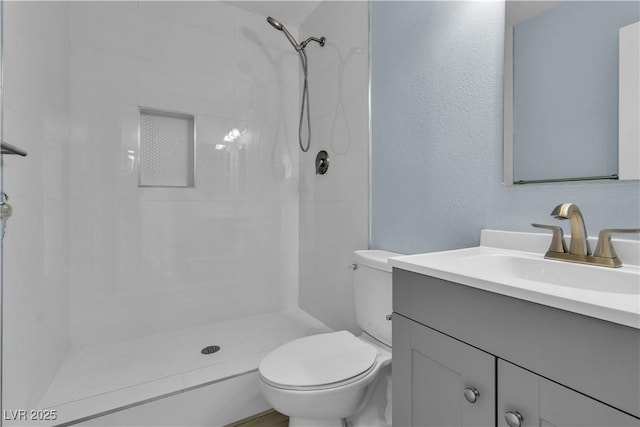 bathroom with vanity, toilet, a shower, and a textured wall