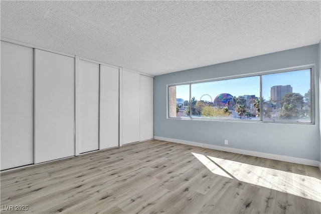 unfurnished room featuring baseboards, light wood-type flooring, and a textured ceiling