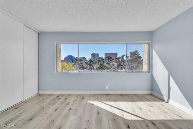 spare room featuring a city view, a textured ceiling, baseboards, and wood finished floors