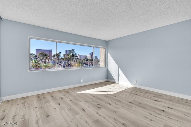 spare room featuring a city view, wood finished floors, baseboards, and a textured ceiling