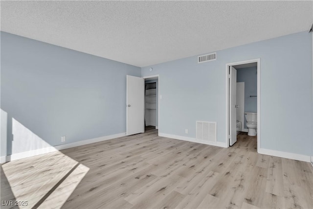 interior space with visible vents, baseboards, light wood-style floors, and a textured ceiling