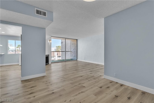 unfurnished room featuring visible vents, baseboards, floor to ceiling windows, wood finished floors, and a textured ceiling