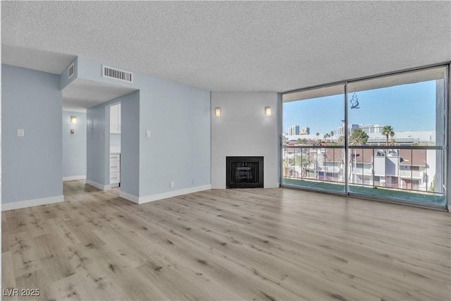 unfurnished living room with visible vents, floor to ceiling windows, a fireplace, wood finished floors, and a textured ceiling