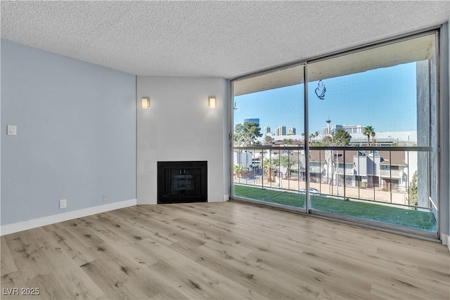 unfurnished living room with a wall of windows, wood finished floors, a fireplace, a textured ceiling, and a view of city