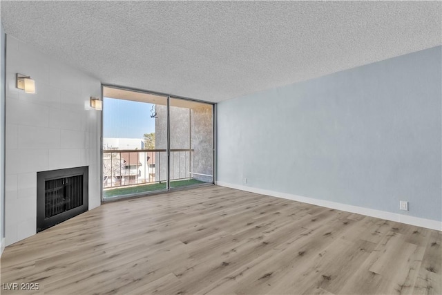 unfurnished living room featuring a wall of windows, baseboards, a textured ceiling, and wood finished floors