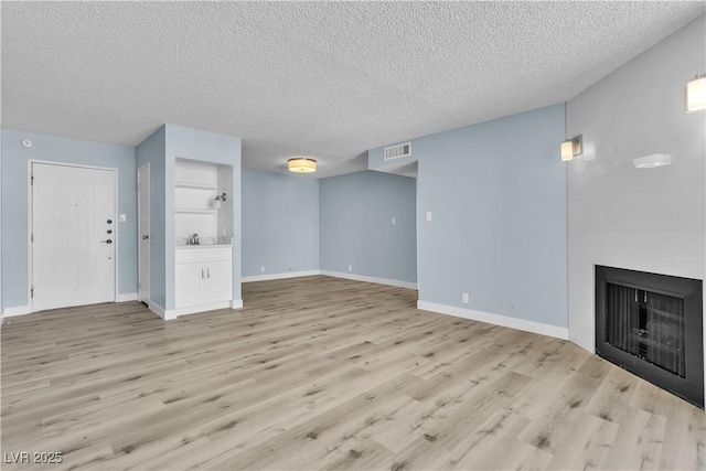 unfurnished living room with light wood-type flooring, visible vents, a textured ceiling, and a fireplace