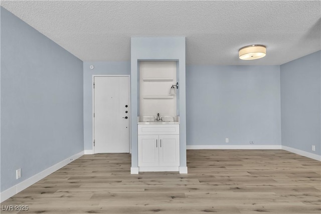 spare room featuring light wood-style flooring, a textured ceiling, baseboards, and a sink