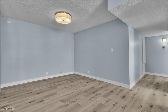 unfurnished room with a textured ceiling, baseboards, and wood finished floors