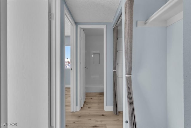 hall with wood finished floors, baseboards, and a textured ceiling