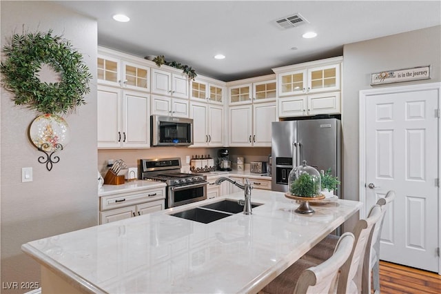 kitchen with visible vents, a center island with sink, a sink, appliances with stainless steel finishes, and a breakfast bar area