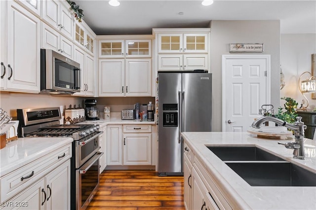 kitchen with a sink, appliances with stainless steel finishes, wood finished floors, and white cabinetry