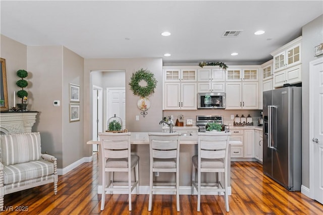 kitchen with visible vents, a center island with sink, wood finished floors, stainless steel appliances, and light countertops