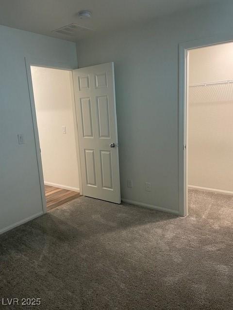 unfurnished bedroom featuring a walk in closet, carpet flooring, and baseboards