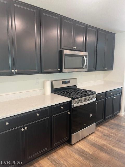 kitchen featuring stainless steel appliances, dark cabinetry, light wood-style flooring, and light countertops