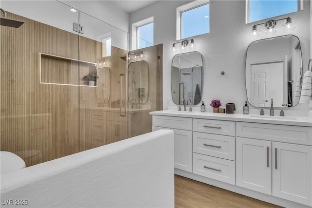 full bathroom with a sink, a shower with door, wood finished floors, double vanity, and a towering ceiling