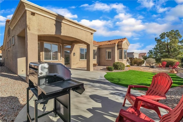 rear view of property featuring a patio, a lawn, a tile roof, and stucco siding