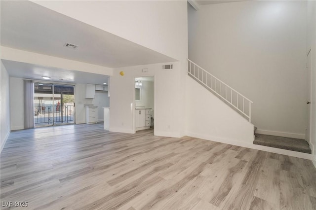 unfurnished living room featuring stairs, light wood-style floors, visible vents, and baseboards