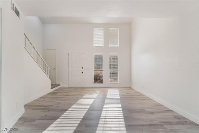 foyer entrance with stairway, visible vents, light wood-style flooring, and a towering ceiling