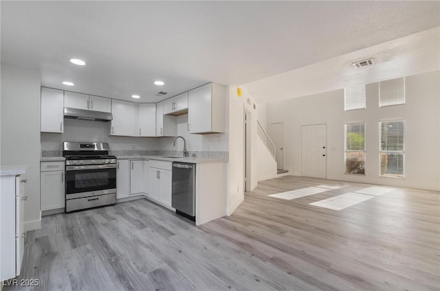 kitchen featuring visible vents, under cabinet range hood, open floor plan, appliances with stainless steel finishes, and a sink