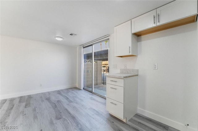 kitchen featuring light wood-type flooring, white cabinetry, light countertops, a wall of windows, and baseboards