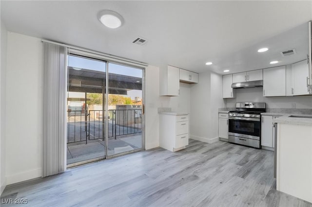 kitchen featuring under cabinet range hood, visible vents, stainless steel gas stove, and white cabinetry