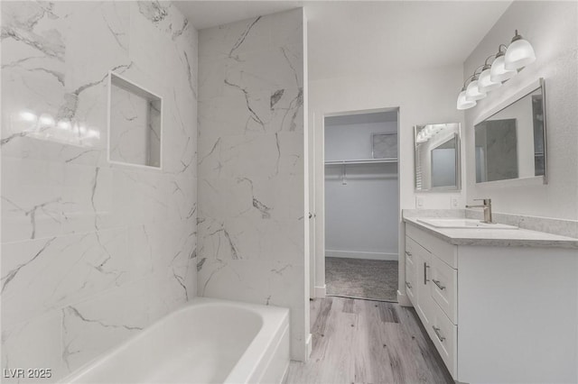 bathroom with a walk in closet, baseboards, a tub to relax in, wood finished floors, and vanity