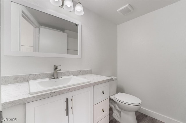 half bathroom featuring visible vents, baseboards, toilet, wood finished floors, and vanity