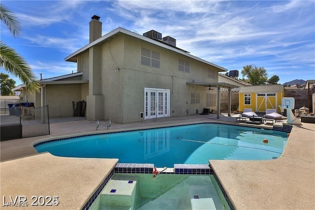 view of swimming pool with a pool with connected hot tub, a patio, fence, french doors, and a storage shed