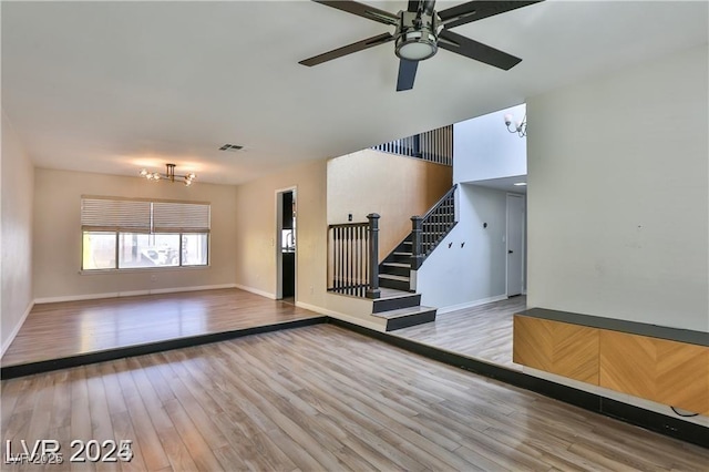 spare room with visible vents, ceiling fan with notable chandelier, wood finished floors, baseboards, and stairs