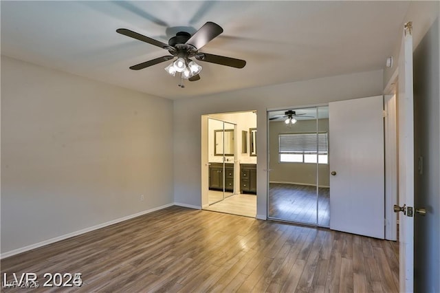 unfurnished bedroom with wood finished floors, connected bathroom, a closet, baseboards, and ceiling fan