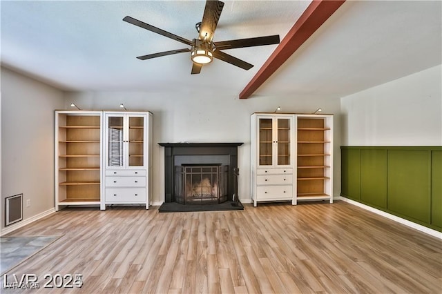 unfurnished living room featuring ceiling fan, beam ceiling, wood finished floors, and a fireplace with raised hearth