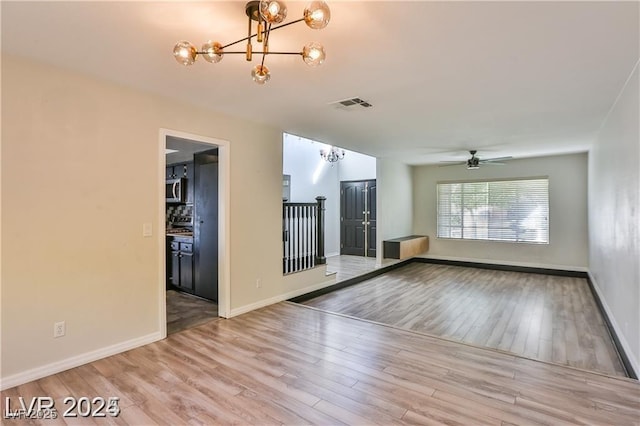 empty room featuring ceiling fan with notable chandelier, wood finished floors, visible vents, and baseboards