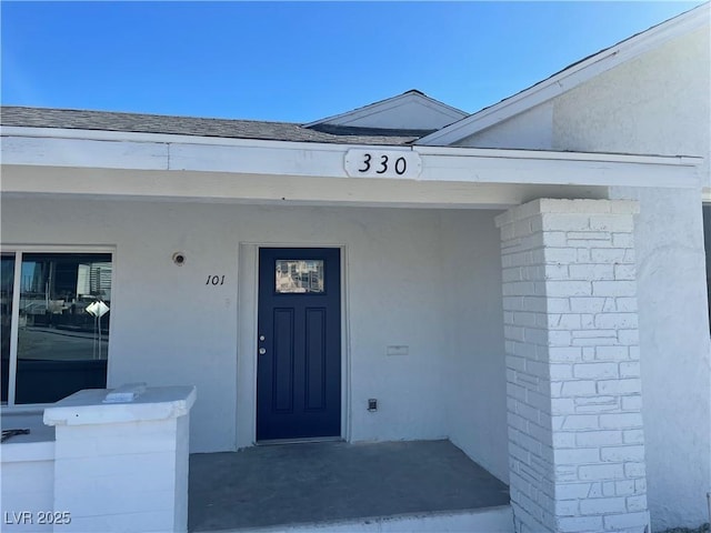 doorway to property featuring roof with shingles and stucco siding