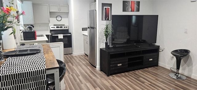 kitchen with baseboards, light wood finished floors, a sink, stainless steel appliances, and light countertops