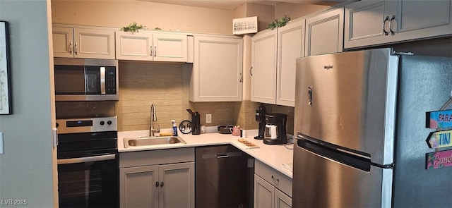 kitchen with tasteful backsplash, light countertops, gray cabinets, appliances with stainless steel finishes, and a sink